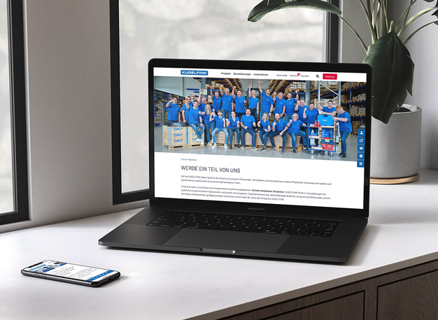 Auf einem Schreibtisch steht ein Laptop, auf dem eine Website mit einem Teamfoto der Mitarbeiter in blauen Uniformen angezeigt wird.