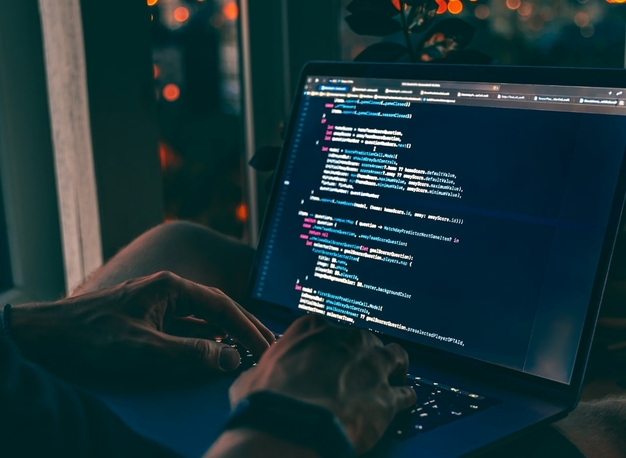 Person, die in einem schwach beleuchteten Raum Code auf einem Laptop eintippt.