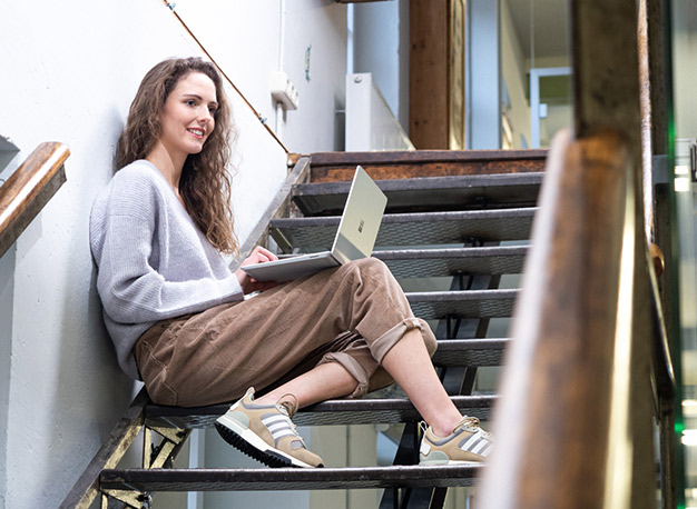 Ein Grafikerin sitzt auf der Treppe und arbeitet am Laptop
